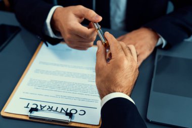 İş anlaşması yapılırken iki işadamı masanın karşısında oturuyor. Şirket avukatı, sözleşmeyi imzalaması için müvekkiline ya da ortağına kalem veriyor ve anlaşmayı imzayla imzalıyor. Coşkulu