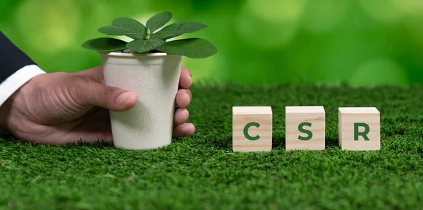Businessman holding plant pot with cube symbolizing CSR. Ethical and eco-friendly green business with no CO2 emission policy. Committed to corporate social responsibility for greener community. Alter