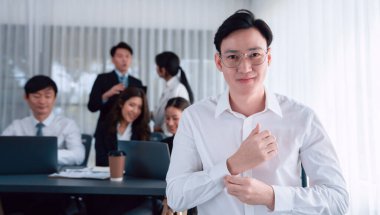 Portrait of focus young successful confident male manager, executive wearing business wear in harmony office arm crossed with blurred meeting background of colleagues, office worker.