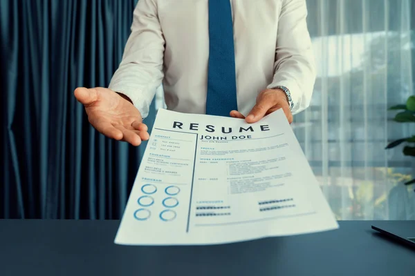 stock image Confident man wearing suit in formal office, hand holding resume paper during job interview. Interviewer point of view with candidate handing resume paper in front of camera for consideration. Fervent