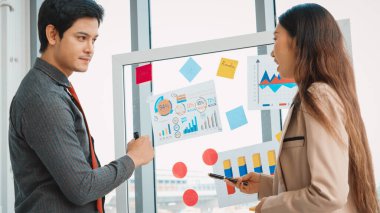 İş adamları ofisteki proje planlama kurulunda çalışıyor ve proje gelişimini analiz etmek için iş arkadaşlarıyla sohbet ediyorlar. Düzenli olması için cama yapıştırılmış yapışkan notlar kullanıyorlar. Jivy