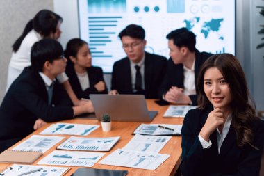 Focus portrait of female manger, businesswoman in the harmony meeting room with blurred of colleagues working together, analyzing financial paper report and dashboard data on screen in background.