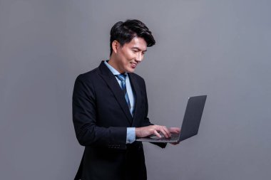 Kendine güvenen genç Asyalı iş adamı dizüstü bilgisayarla izole edilmiş arka planda poz veriyor. Ofis çalışanı yenilikçi ürün reklamları, tanıtım satışları veya insan kaynakları için el ele tutuşuyor. Sevinçli.