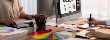 Grafik tasarımcısı, modern dijital stüdyo işyerinde profesyonel grafik ekibiyle benzersiz bir tasarım yaparken bilgisayar dizüstü bilgisayar ve grafik çizim kalemi üzerinde çalışır. Panorama çekimi. İnceleyin