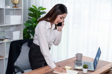 Genç hevesli iş kadını iş görüşmesinde konuşuyor ve laptopuna çoklu ofis hanımı olarak notlar yazıyor. Müşterilerle telefonda konuşurken iş ödevleri yazan kadın çalışan.