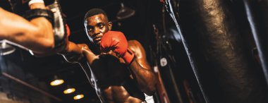 Spor salonunda boks çantası olarak boks eldiveni takan Afrikalı boksör antrenörleri yumrukluyor. Profesyonel boks maçı için güç ve dayanıklılık eğitimi. Mahmuz