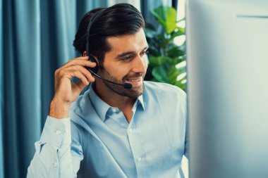 Erkek çağrı merkezi operatörü ya da telesales temsilcisi ofis masasında oturmuş kulaklık takıyor ve müşteri hizmetleri desteği sağlayan ya da satış yapan müşteriyle sohbet ediyor. coşkulu