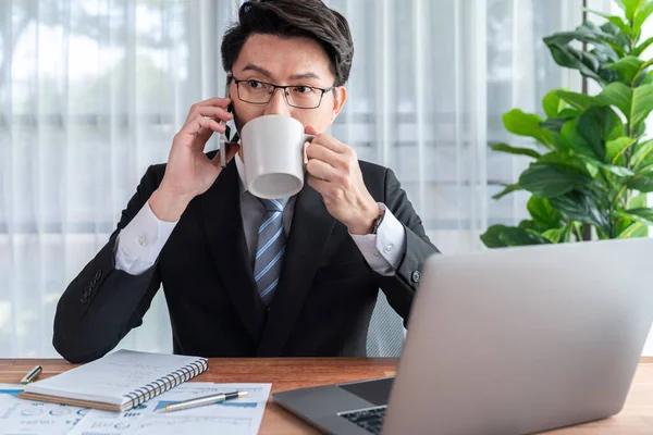 stock image Businessman working on laptop for on office desk workspace with his smartphone. Smart executive researching financial business data or planning strategic business, talking on phone. Jubilant