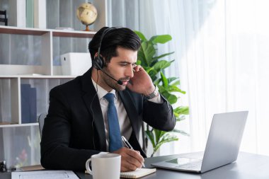 Erkek çağrı merkezi operatörü ya da telesales temsilcisi ofis masasında oturmuş kulaklık takıyor ve müşteri hizmetleri desteği sağlayan ya da satış yapan müşteriyle sohbet ediyor. coşkulu