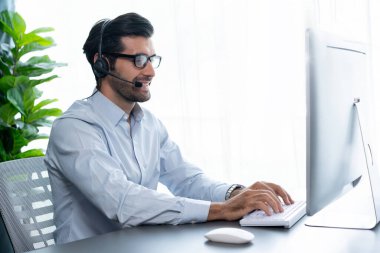 Erkek çağrı merkezi operatörü ya da telesales temsilcisi ofis masasında oturmuş kulaklık takıyor ve müşteri hizmetleri desteği sağlayan ya da satış yapan müşteriyle sohbet ediyor. coşkulu