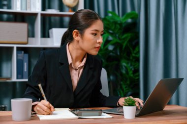 Genç Asyalı iş kadını özenle çalışıyor ve modern ofis çalışma alanında notlar alıyor. Çekici ve çalışkan bir ofis hanımı olarak profesyonelliğini gösteriyor. Coşkulu.