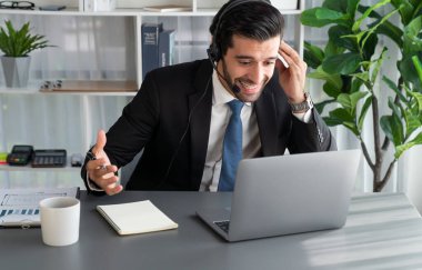 Erkek çağrı merkezi operatörü ya da telesales temsilcisi ofis masasında otururken kulaklık takıyor ve müşteri desteği sağlayan ya da ikna edici satış yapan müşteriyle sohbet ediyor. coşkulu