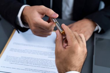 İş anlaşması yapılırken iki işadamı masanın karşısında oturuyor. Şirket avukatı, sözleşmeyi imzalaması için müvekkiline ya da ortağına kalem veriyor ve anlaşmayı imzayla imzalıyor. Coşkulu