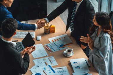 Grup iş adamları toplantı masasında el sıkışırken üst açıdan kendilerine güvenirler. Genç işadamı ve işkadını işçiler yatırım anlaşması imzaladılar. Jivy