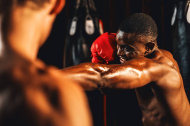 Afrika kökenli siyah boksör antrenöre yumruk atıyor ya da spor salonunda boks çantası olarak boks eldiveni takıyor. Profesyonel boks maçı için güç ve dayanıklılık eğitimi. Impetus