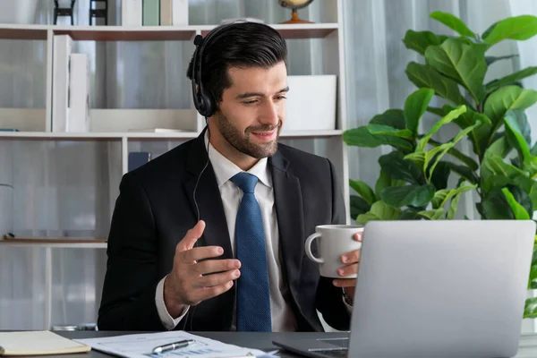 stock image Manager of call center operator office sitting on his desk with his coffee while working on laptop. Office worker wearing headset and black suit working on customer support or telemarketing. fervent