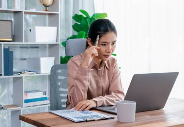 Modern ofis masasındaki Asyalı hevesli genç iş kadını çalışmak ve notlar yazmak için dizüstü bilgisayar kullanıyor. Çalışkan ve çekici ofis hanımı ofisinde bilgisayar defteri üzerinde çalışıyor..