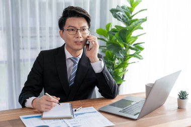 Ofis masasında akıllı telefonuyla bilgisayar başında çalışan bir iş adamı. Akıllı bir yönetici finansal iş verilerini araştırıyor ya da stratejik işler planlıyor, telefonla konuşuyor. Sevinçli.