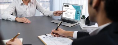 Aday ve mülakatçı, kurumsal ofiste iş deneyimi ve niteliklerini tartışıyor. İK ekibi iş başvurusunu dizüstü bilgisayardan değerlendirirken sorgulanan kişi de profilini açıklıyor. Dahi.