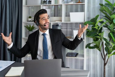 Erkek çağrı merkezi operatörü ya da telesales temsilcisi ofis masasında otururken kulaklık takıyor ve müşteri desteği sağlayan ya da ikna edici satış yapan müşteriyle sohbet ediyor. coşkulu