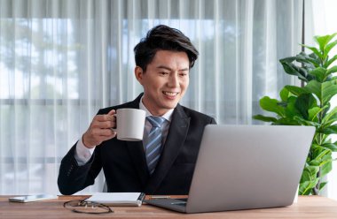 Ofis masasında dizüstü bilgisayarda çalışan bir iş adamı. Akıllı yönetici finansal iş verilerini araştırıyor ya da masada bilgisayarla stratejik iş pazarlaması planlıyor. Sevinçli.