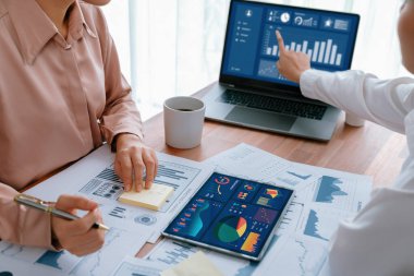 Analist ekip arkadaşı dijital gösterge panelinde finansal verileri tartışır, grafikleri dizüstü bilgisayar ve tablet ekranda analiz eder. Modern ofis pazarlama planlamak için iş zekasını kullanır. Coşkulu.