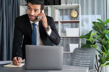 Çalışkan işadamı, ofisindeki dizüstü bilgisayarla cep telefonlu, modern, çalışkan ofis çalışanı yaşam biçimi konsepti olarak çalışırken müşterileriyle telefonda konuşmakla meşgul. Coşkulu