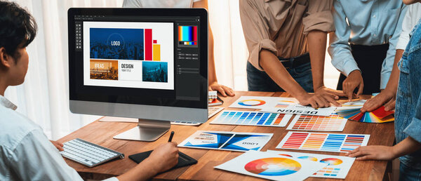 Graphic designer work on computer laptop and with graphic drawing pen while brainstorming unique design with professional graphic team in modern digital studio workplace. Panorama shot. Scrutinize