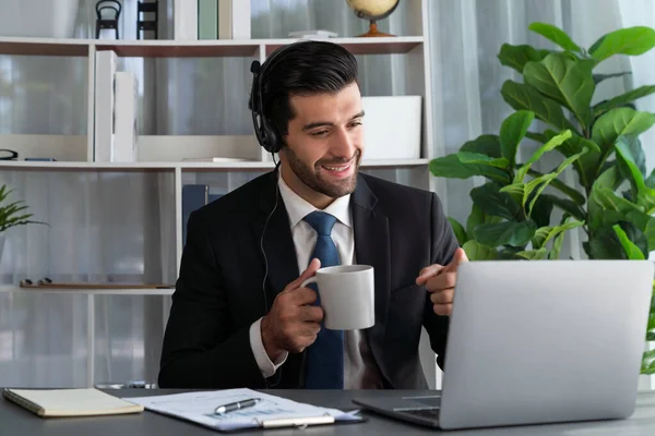 stock image Manager of call center operator office sitting on his desk with his coffee while working on laptop. Office worker wearing headset and black suit working on customer support or telemarketing. fervent