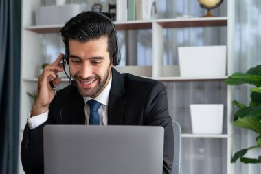 Erkek çağrı merkezi operatörü ya da telesales temsilcisi ofis masasında otururken kulaklık takıyor ve müşteri desteği sağlayan ya da ikna edici satış yapan müşteriyle sohbet ediyor. coşkulu