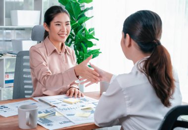 İki Asyalı iş kadını, iş yeri konseptinde takım çalışması ve dürüstlüğün önemi olarak, gösterge paneli veri kağıtlarının yığınlarını başarıyla analiz ettikten sonra modern ofiste el sıkışıyor. Coşkulu.