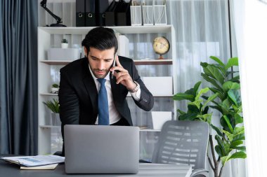 Çalışkan işadamı, ofisindeki dizüstü bilgisayarla cep telefonlu, modern, çalışkan ofis çalışanı yaşam biçimi konsepti olarak çalışırken müşterileriyle telefonda konuşmakla meşgul. Coşkulu