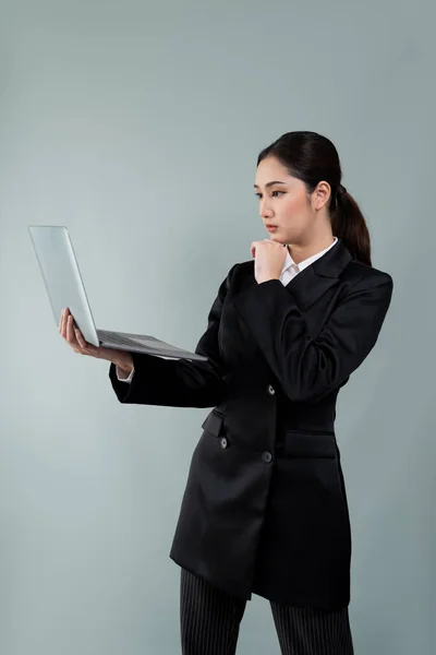 stock image Confident young businesswoman stands on isolated background, working on laptop posing in formal black suit. Office lady or manager with smart and professional appearance. Enthusiastic