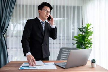 Ofis masasında akıllı telefonuyla bilgisayar başında çalışan bir iş adamı. Akıllı bir yönetici finansal iş verilerini araştırıyor ya da stratejik işler planlıyor, telefonla konuşuyor. Sevinçli.