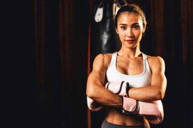 Asya 'lı kadın Muay Thai boksörü kamera önünde boksör yumruğu. Arka planda boks ekipmanıyla spor salonunda poz vermeye hazır. Kararlı gözler ve meydan okumaya hazır olun. Impetus