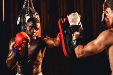 Afrika kökenli siyah boksör antrenöre yumruk atıyor ya da spor salonunda boks çantası olarak boks eldiveni takıyor. Profesyonel boks maçı için güç ve dayanıklılık eğitimi. Impetus