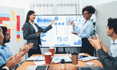 İş adamları TV ekranında başarılı bir sunum veya veri analizi toplantısından sonra kutlama yapıyorlar. Mutlu takım ofis odasında toplanıyor, kutlama jestleriyle işbirliği için tezahürat yapıyorlar. Uyum