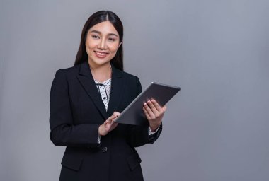 Kendine güvenen Asyalı genç iş kadını izole edilmiş arka planda tabletle poz veriyor. Ofisteki bayan tanıtım, satış, teknoloji ve yenilik ürünleri reklamları için el ele tutuşuyor. Sevinçli.