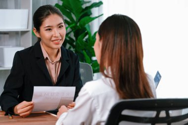 İki Asyalı kadın ofiste iş görüşmesi yapıyor. Başvuranlar özgeçmişi ve iş başvurusu hakkında konuşurken resmi takım giyerler. Muhabir olumlu ve konuşkan bir şekilde sorgulama talep ediyor. Coşkulu.