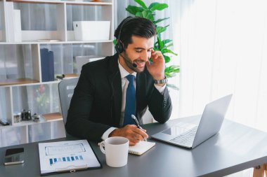 Erkek çağrı merkezi operatörü ya da telesales temsilcisi ofis masasında oturmuş kulaklık takıyor ve müşteri hizmetleri desteği sağlayan ya da satış yapan müşteriyle sohbet ediyor. coşkulu