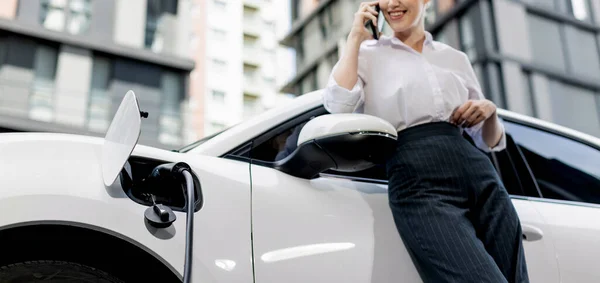 Closeup Progressive Businesswoman Smartphone Leaning Electric Car Charging Station Driving — Foto Stock