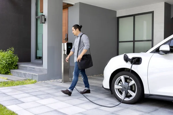 stock image Progressive asian man and electric car with home charging station. Concept of the use of electric vehicles in a progressive lifestyle contributes to a clean and healthy environment.