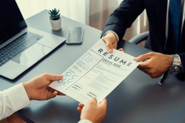 Resmi ofiste takım elbise giyen kendine güvenen bir adam, iş görüşmesi sırasında özgeçmiş kağıtlarını tutuyor. Sorular soran, aday yeterliliği ve iş için uygunluk değerlendirmesi yapan bir muhabir. Coşkulu