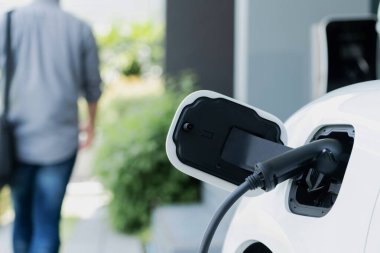 Focus electric car charging at home charging station with blurred progressive man walking in the background. Electric car using renewable clean for eco-friendly concept.
