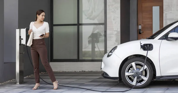 Progressive Asian Woman Holding Smartphone Electric Car Home Charging Station — Photo