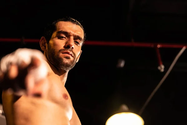 stock image Boxing fighter shirtless posing, caucasian boxer punch his bare fist and wrap in front of camera, aggressive stance and ready to fight at the boxing ring. Impetus