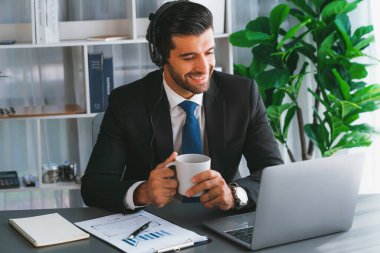 Erkek çağrı merkezi operatörü ya da telesales temsilcisi ofis masasında otururken kulaklık takıyor ve müşteri desteği sağlayan ya da ikna edici satış yapan müşteriyle sohbet ediyor. coşkulu