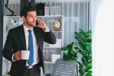 Çalışkan ve meşgul iş adamı modern ofisteki iş arkadaşıyla telefonda konuşuyor. Elinde kahveyle müşteriyle satış görüşmeleri yapmak, profesyonel ofis çalışanı gibi davranmak. Coşkulu