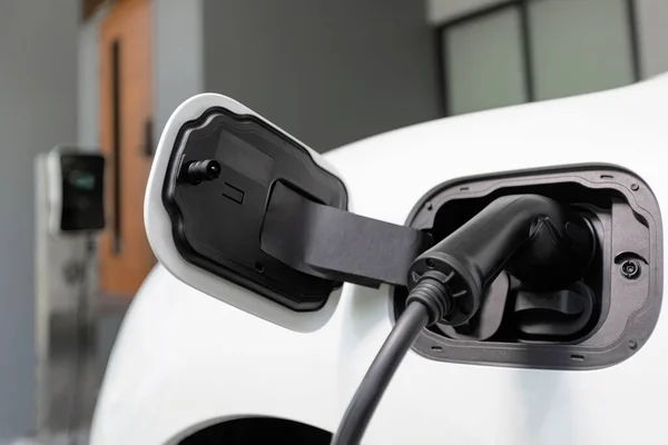 stock image Closeup electric vehicle plugged-in with cable from charging point powered for progressive concept by alternative clean energy rechargeable EV car at home charging station.