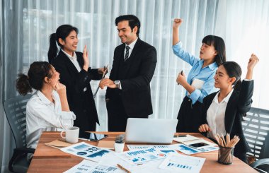 Kutlama jesti ve başarılı takım çalışması yapan bir grup mutlu iş adamı. Çeşitli yarış bürosu çalışanları şirket ofisinde pazarlama planlamasında ilerleme kaydettikten sonra kutlama yapıyorlar. Habiliment